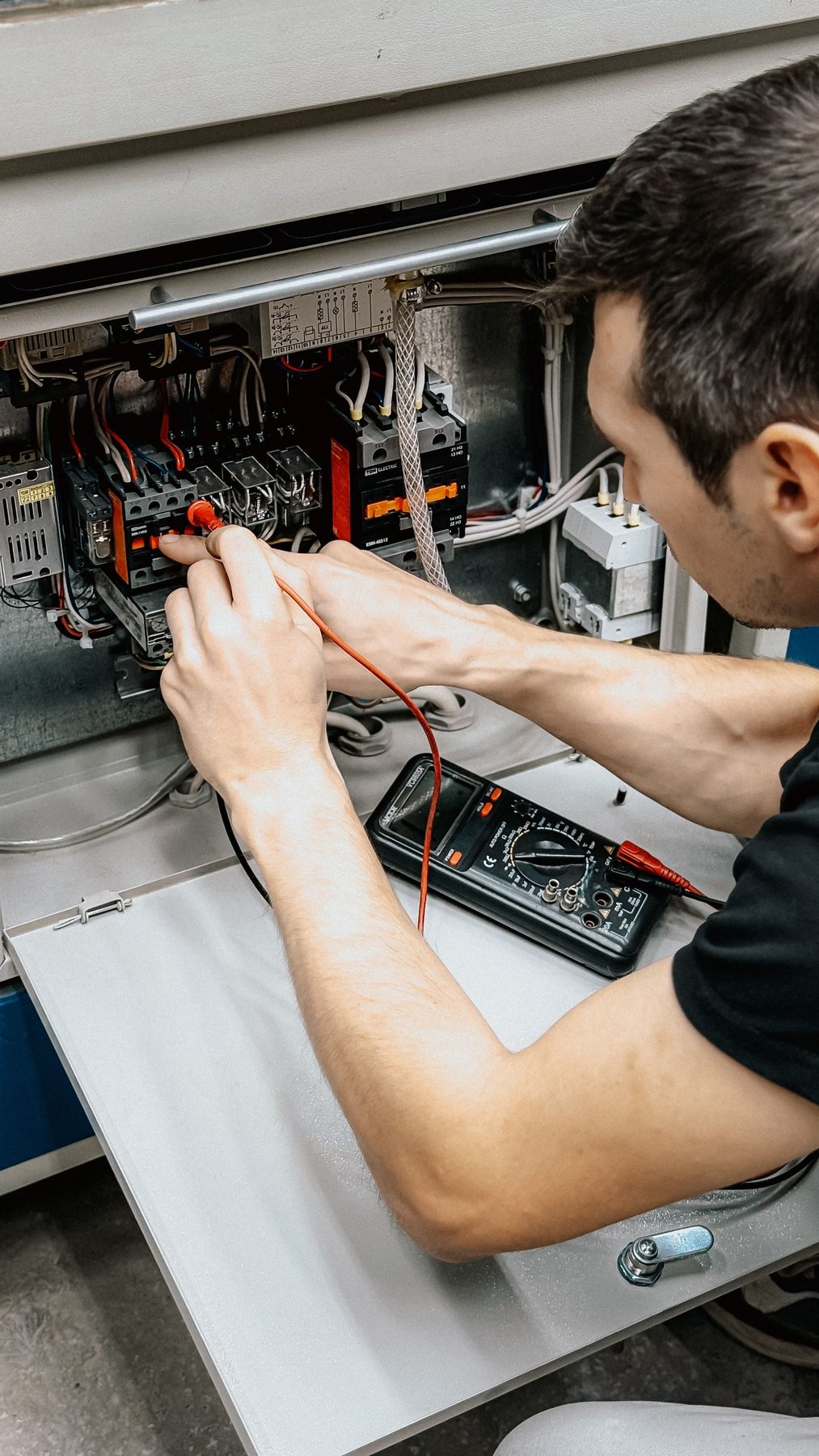Técnico realizando diagnóstico com multímetro em painel de comando elétrico