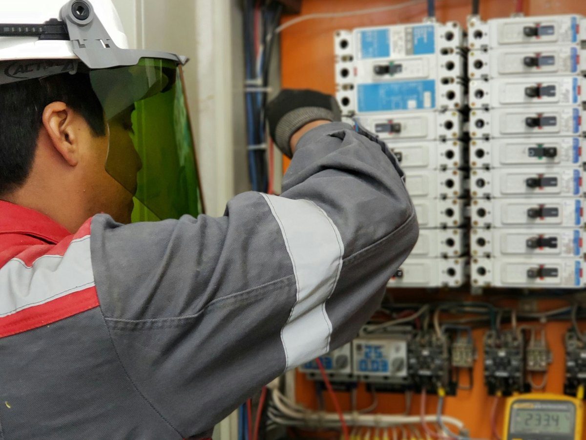Técnico realizando inspeção e manutenção preventiva em quadro elétrico com multímetro